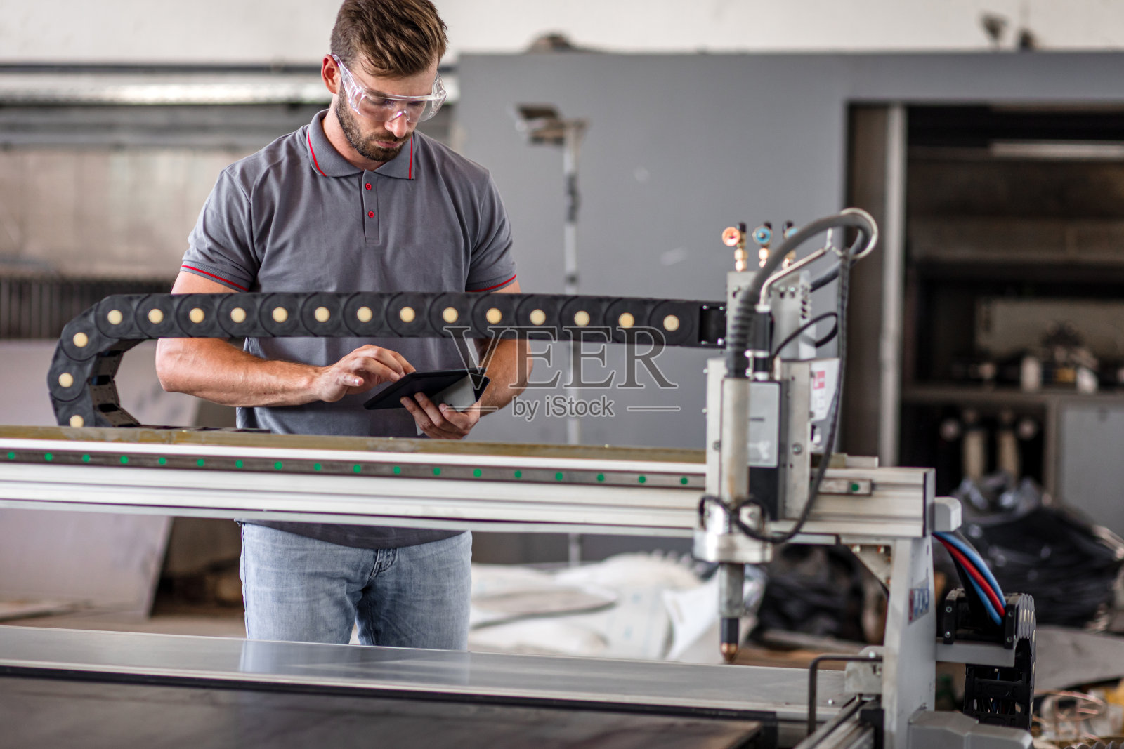 年轻工程师在金属加工车间安装等离子切割机。照片摄影图片