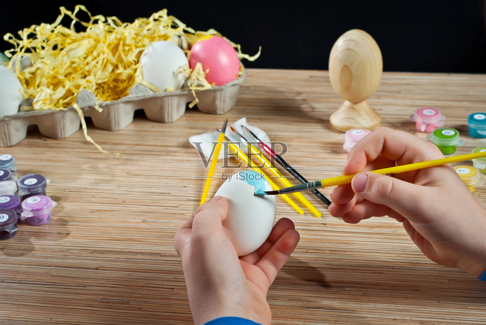 那个男孩画一个复活节彩蛋。手拿蓝色颜料的白色鸡蛋。照片摄影图片