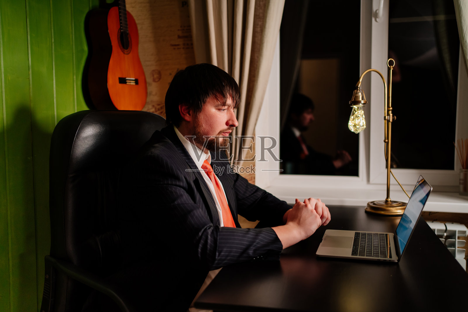 一个穿夹克、打领带的男人晚上在家庭办公室的电脑前工作照片摄影图片