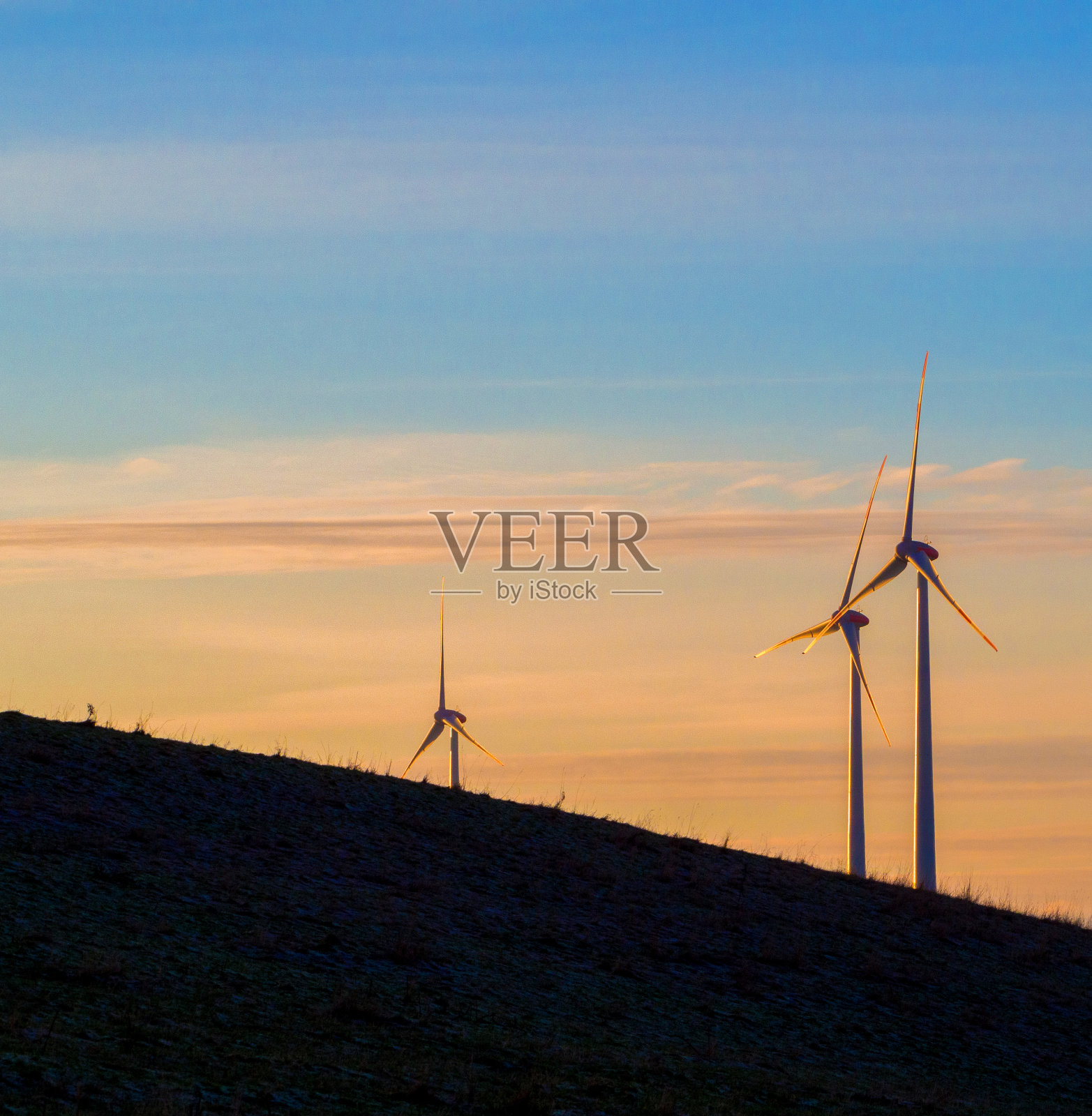 在夕阳的照耀下，场地上矗立着三个风力涡轮机照片摄影图片