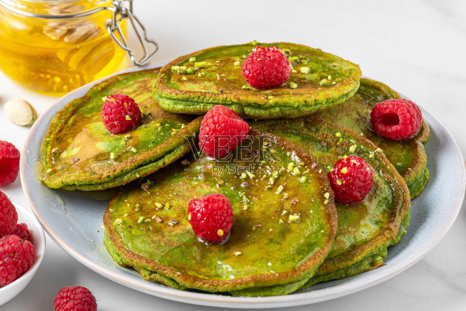 绿色抹茶自制煎饼，配上新鲜的覆盆子、开心果和蜂蜜。近距离照片摄影图片
