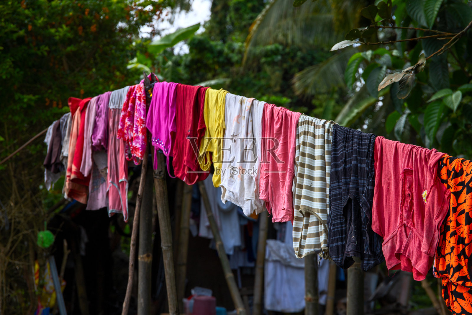 五彩缤纷的衣服挂在绿色的花园里。亚洲村的五彩纺织服装。乡村生活方式的卫生。南亚的社会问题。大家族洗衣服日照片摄影图片