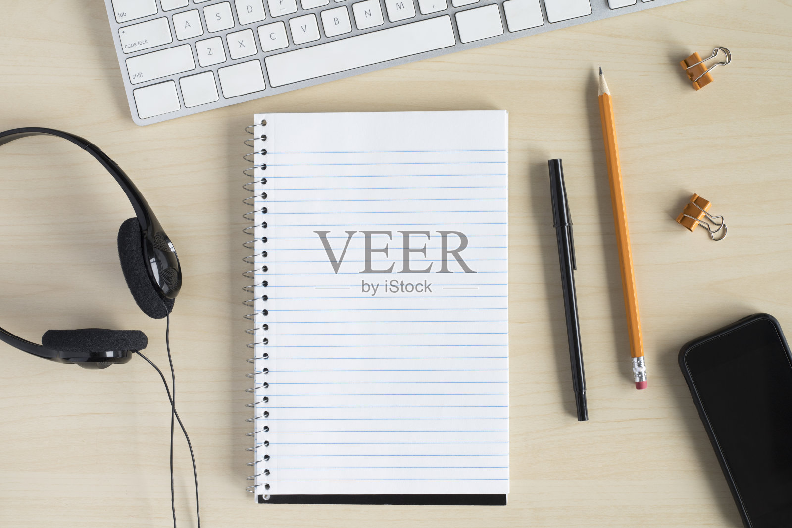 平躺在办公桌上，用电脑键盘、耳机、记事本和文具。照片摄影图片