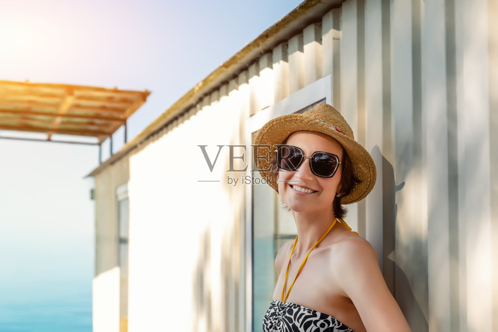 年轻的成年人迷人苗条性感的女人穿着黑白色条纹泳衣，草帽和太阳眼镜对着甲板墙看一边站在木头古董码头。暑假放松照片摄影图片