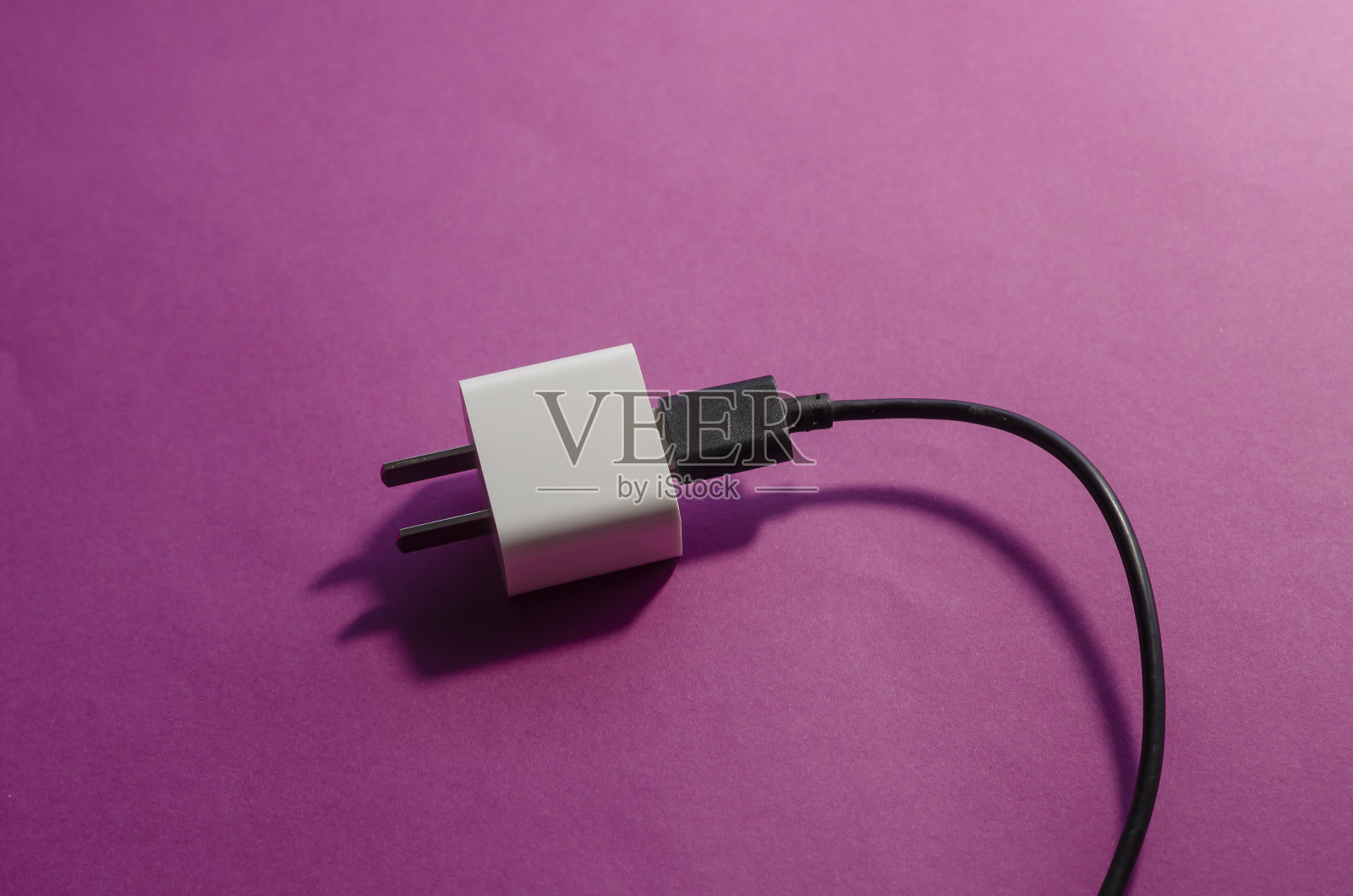 白色智能手机充电器适用于美国与黑色日期电缆在粉红色的背景。照片摄影图片