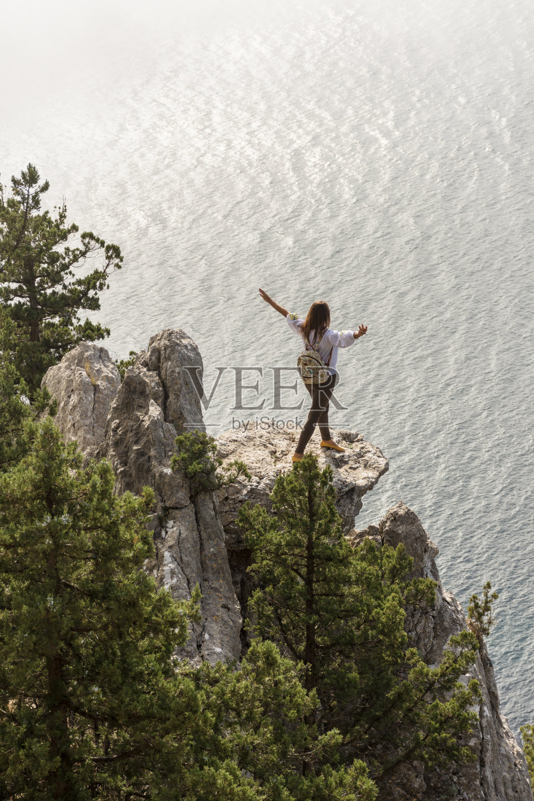 一个快乐的女孩张开双臂站在悬崖边欣赏美丽的景色。照片摄影图片