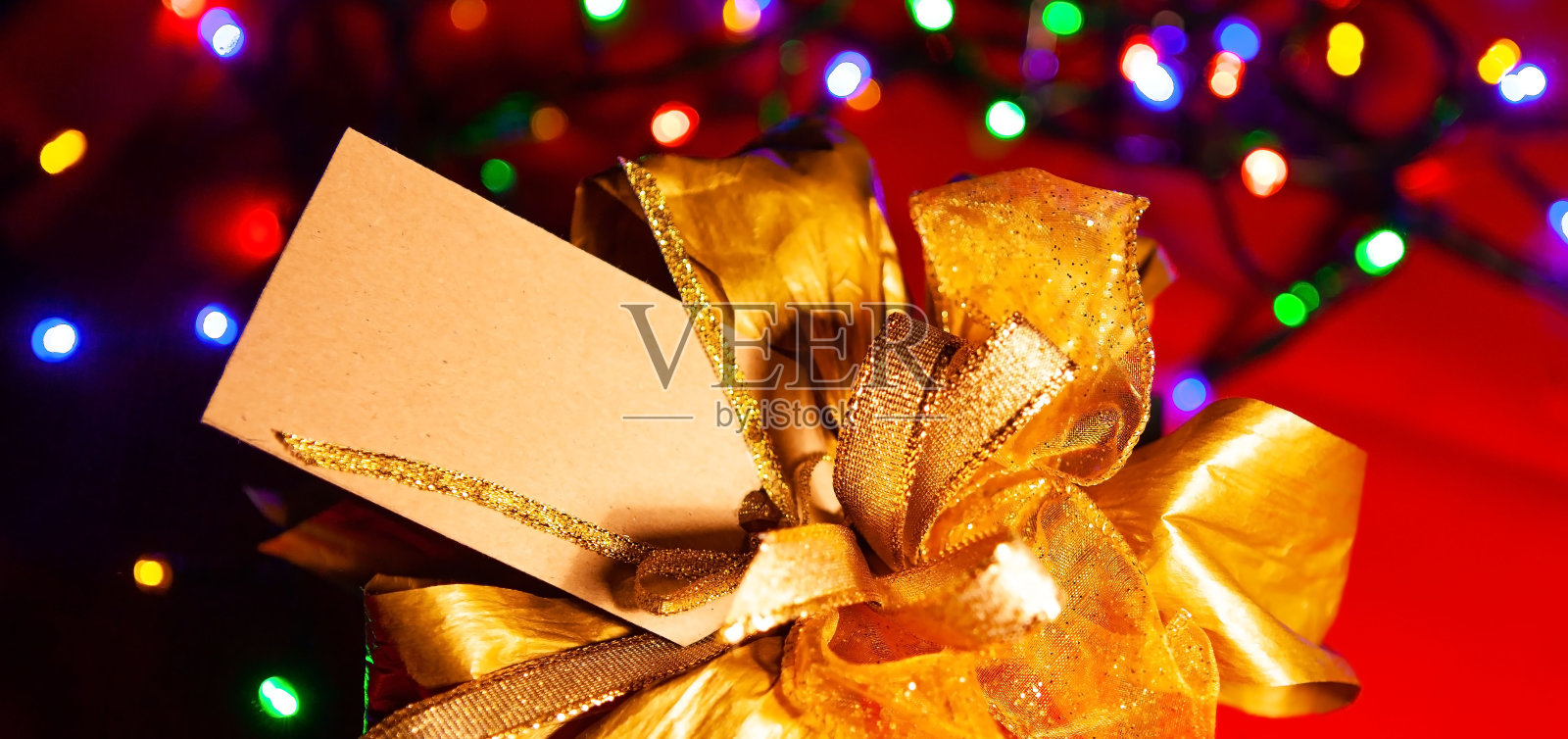 金蝴蝶结上的礼品盒为文字标签，彩灯花环为背景，特写，俯视图。照片摄影图片