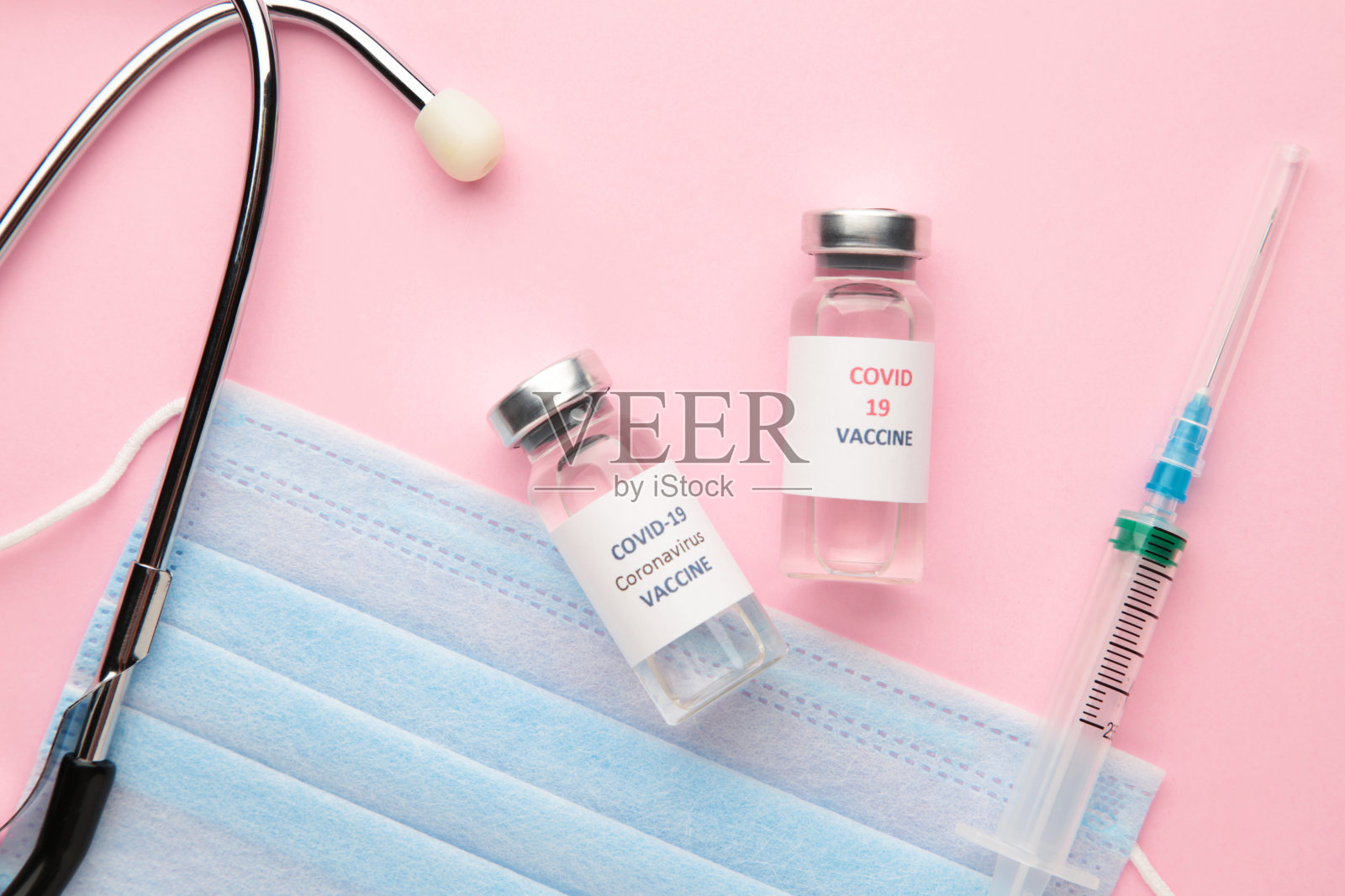 粉红色背景上的新冠肺炎疫苗瓶、注射器和听诊器。接种疫苗和提高免疫力。Covid 19照片摄影图片