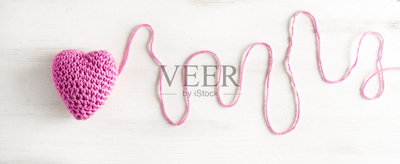 用一根长长的未剪线在白色木制横幅上编织了一颗粉红色的心。照片摄影图片