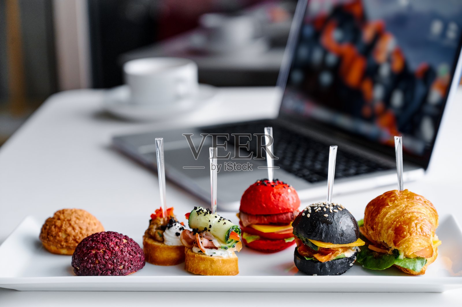 商务午餐在办公室里，零食饼干放在笔记本电脑旁边的白色木桌上。休息时间吃点心照片摄影图片