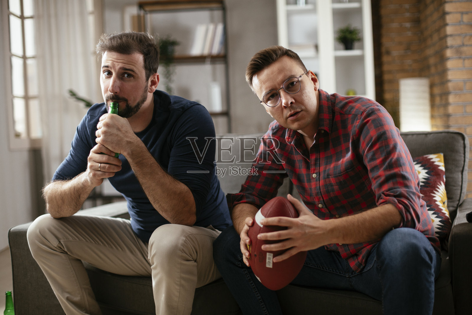 男人喝啤酒，看电视上的体育比赛。照片摄影图片