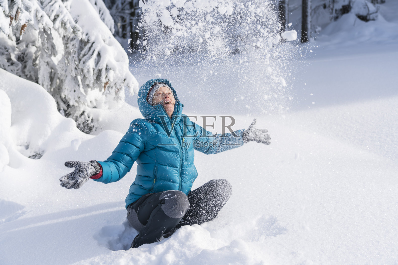 在冬天的森林里，成熟的女人穿着皮大衣向空中抛雪照片摄影图片