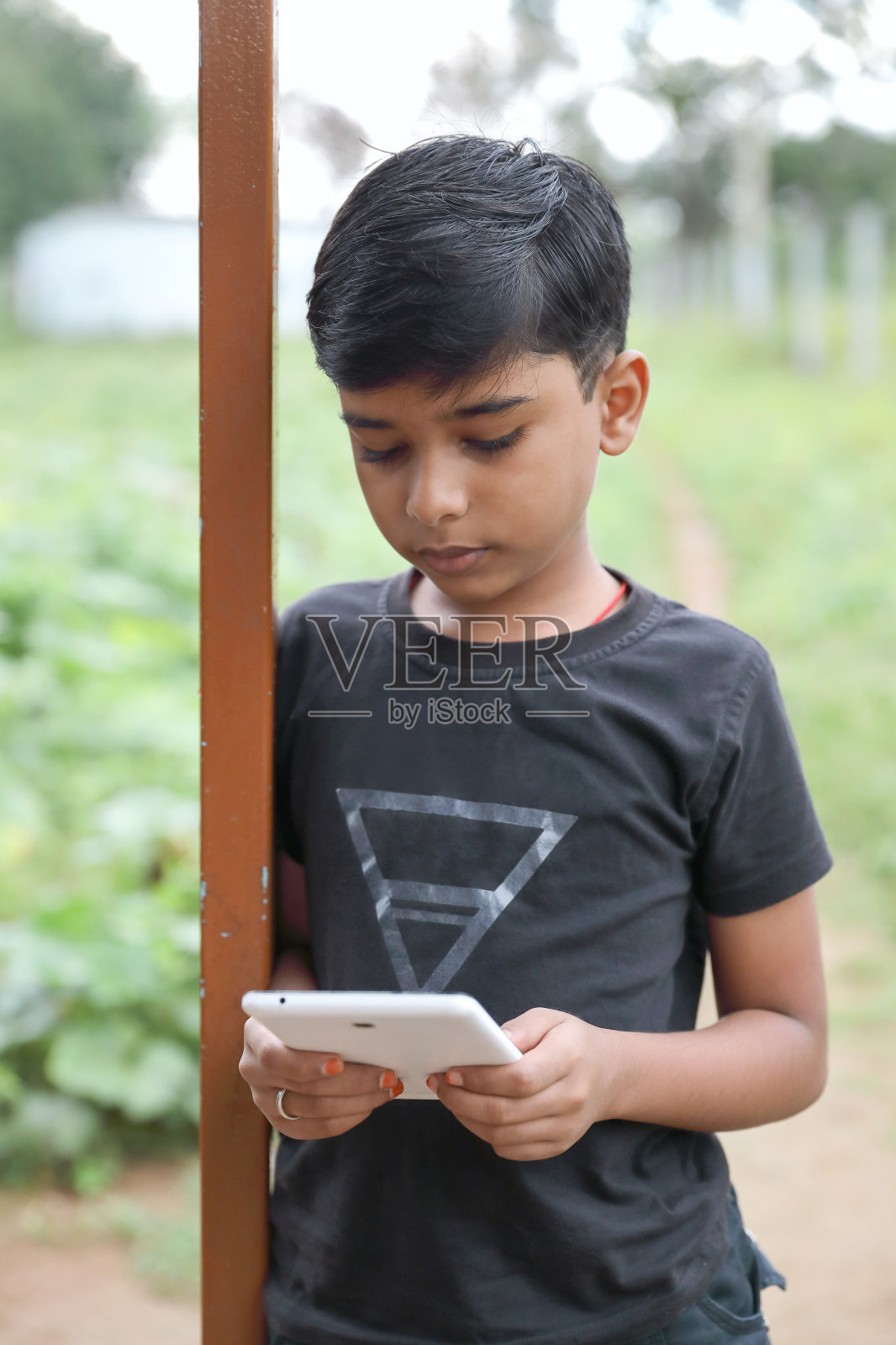 一个印度小男孩在家里使用数字平板电脑，在外面的自然环境中参加在线课程照片摄影图片