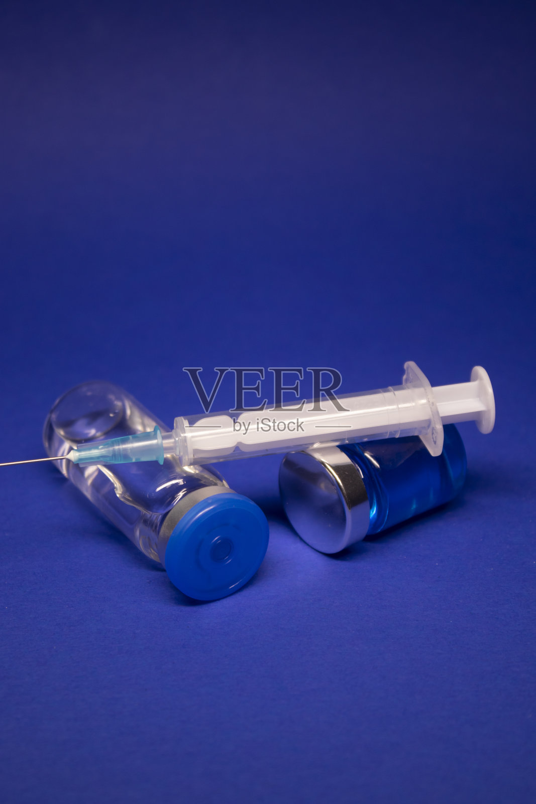 两个透明的无标签疫苗瓶，医用注射器注射针。孤立在蓝色背景。COVID-19冠状病毒疫苗的开发。治疗。世界研究竞赛照片摄影图片