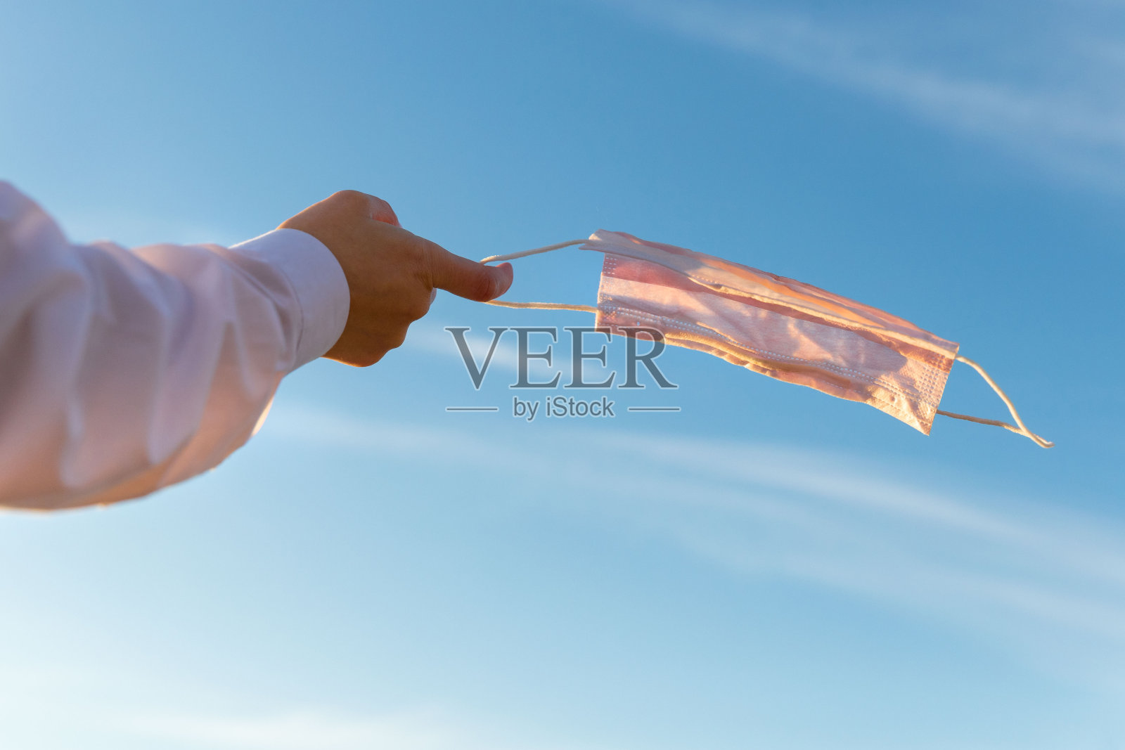 一名妇女摘下医用防护口罩，戴在手指上，头顶蓝天，享受新冠肺炎疫情后的生活和清新空气照片摄影图片