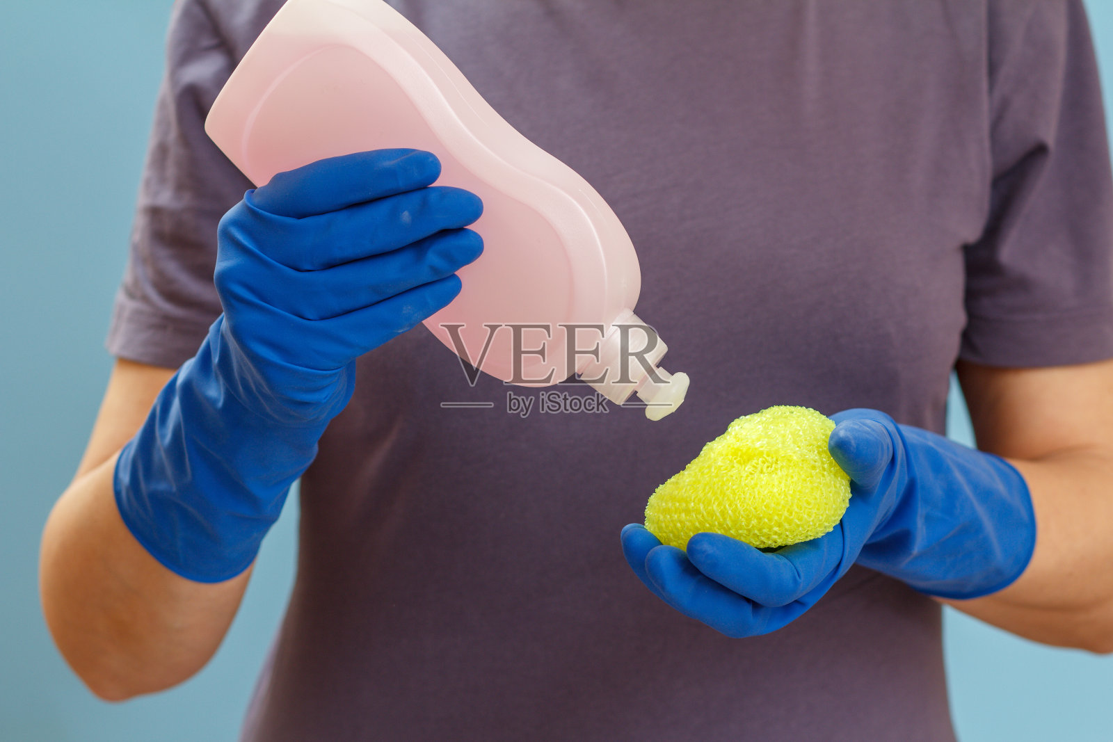 一个女人拿着一瓶洗洁精和一块海绵在蓝色的背景上。照片摄影图片