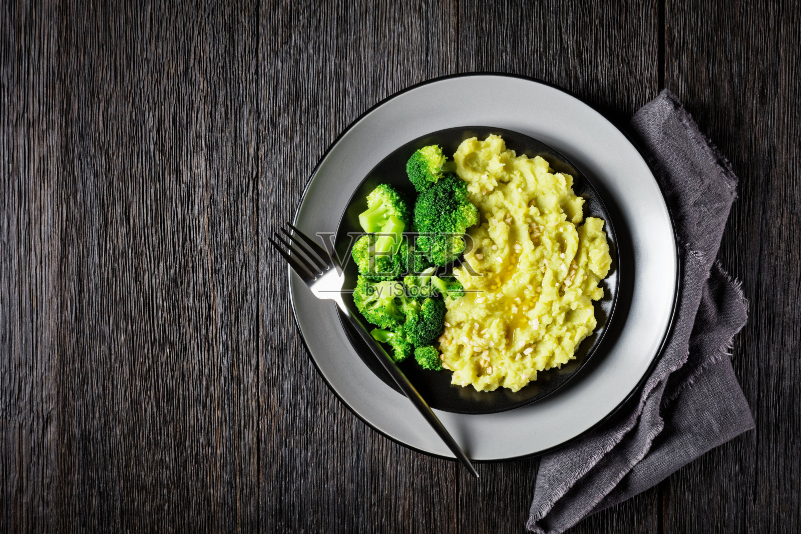 在黑色木桌上的黑色盘子上，撒上花椰菜土豆泥，配上蒸熟的花椰菜小花照片摄影图片