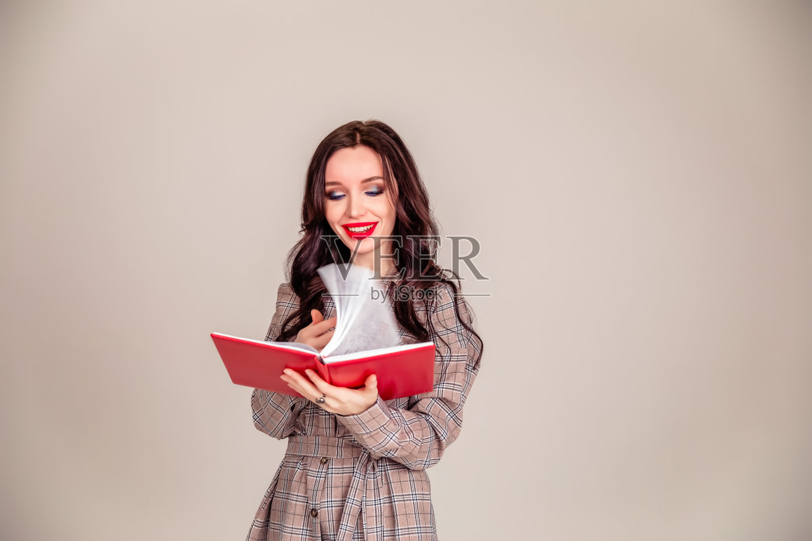 一个漂亮的小女孩，红唇，手里拿着一个红色的笔记本。学生。女商人孤立的灰色背景照片摄影图片