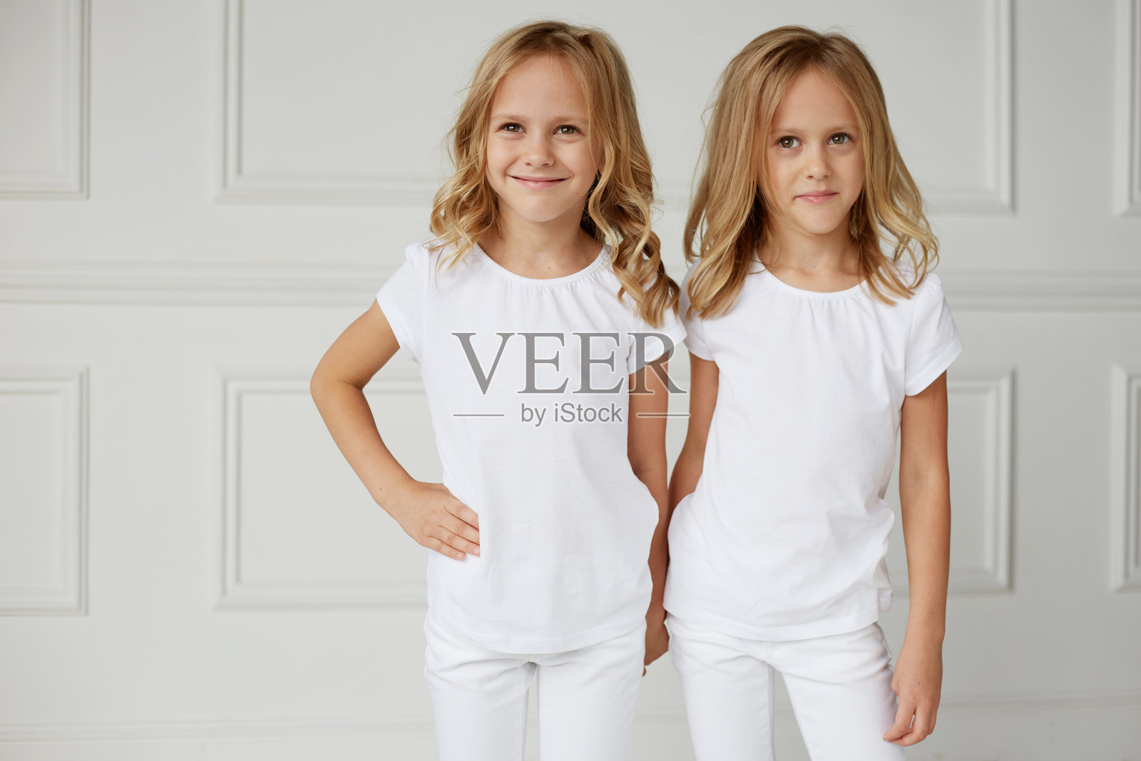 两个穿着白色衣服的小女孩被孤立在白色背景上。双胞胎女孩手牵着手。照片摄影图片