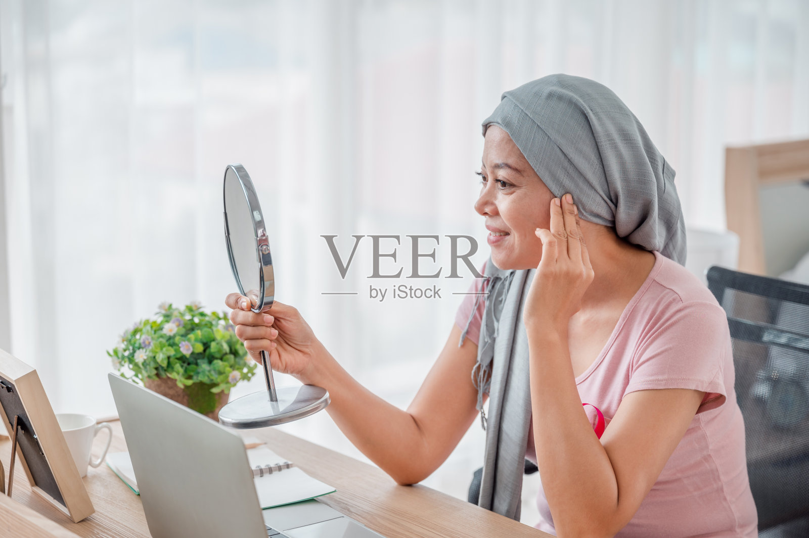 在办公桌前照镜子代表着从乳腺癌中康复。乳腺癌概念，预防癌症概念。照片摄影图片