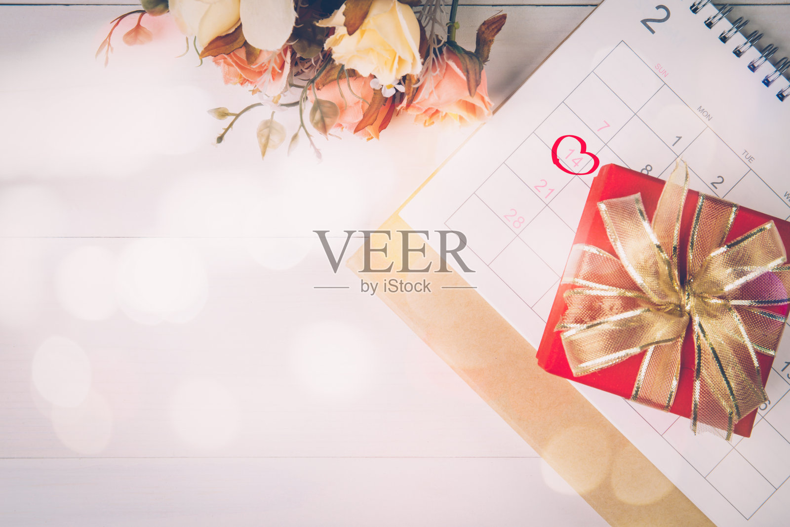 日历和鲜花与备忘录2月14日情人节的办公桌上模糊的散景背景，提醒爱的惊喜，浪漫和甜蜜，庆祝和装饰，俯视图，假日概念。照片摄影图片