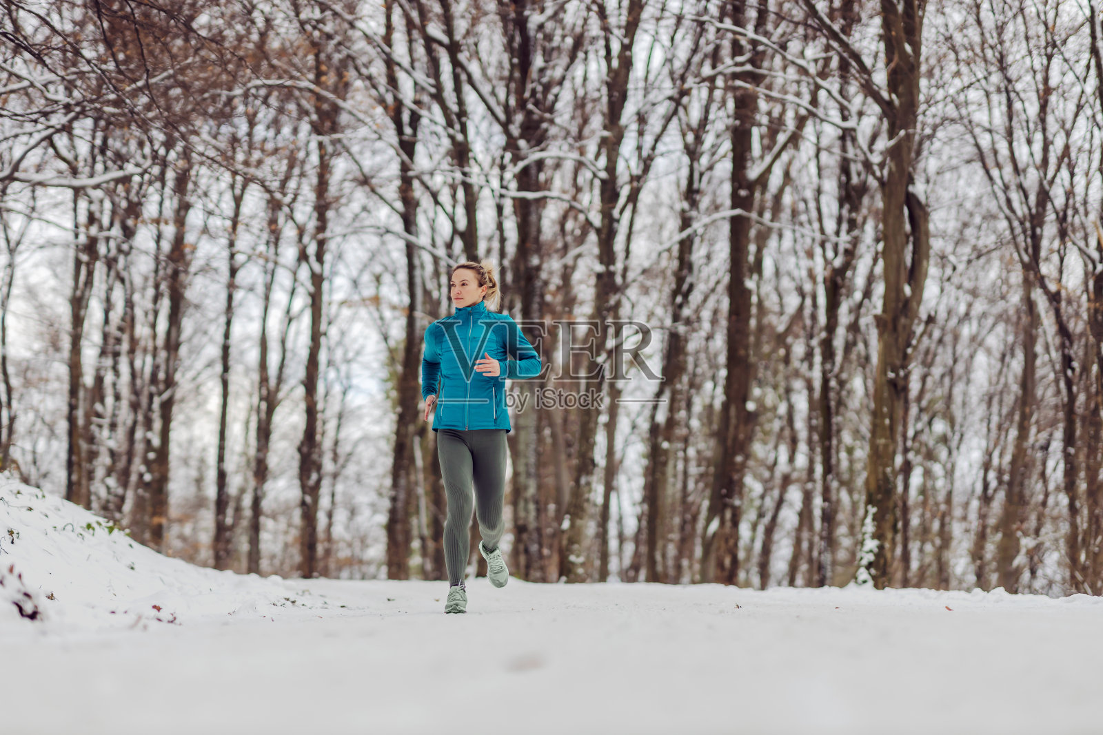 雪天里，苗条的女运动员在森林里慢跑。天气冷，下雪，健康生活，健身，健康习惯，自然照片摄影图片