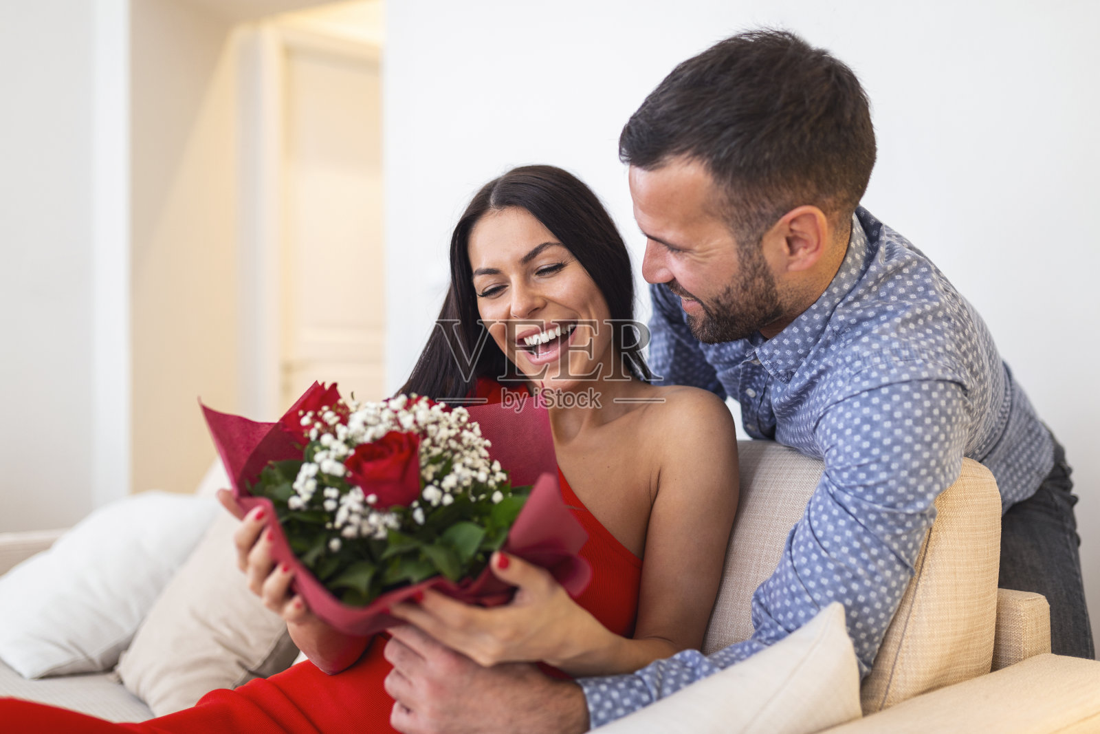 激动的年轻女子收到意想不到的一束红玫瑰从丈夫在家里，爱慷慨的男朋友制造浪漫惊喜迷人的女朋友在情人节的场合照片摄影图片