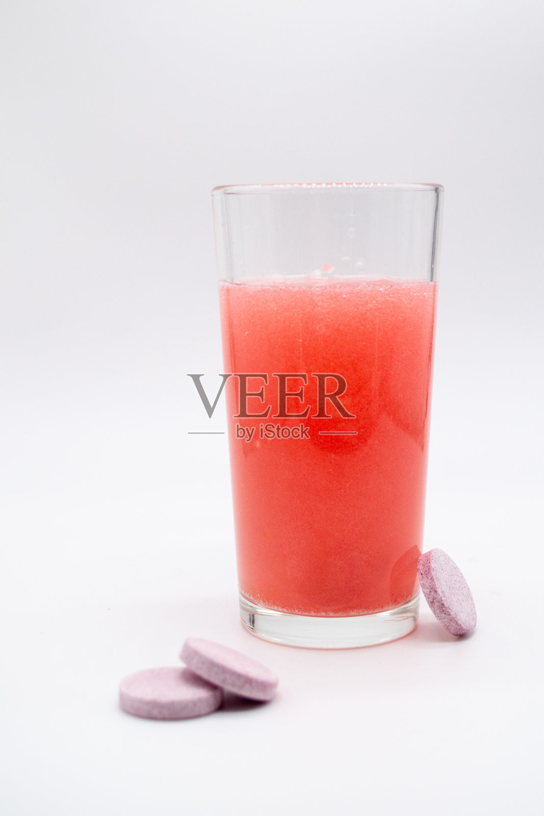 在一杯粉红色的红色水，可溶解，即时或溶解的粉红色药片泡沫。旁边是类似的药片:维生素C，膳食补充剂，止痛药照片摄影图片