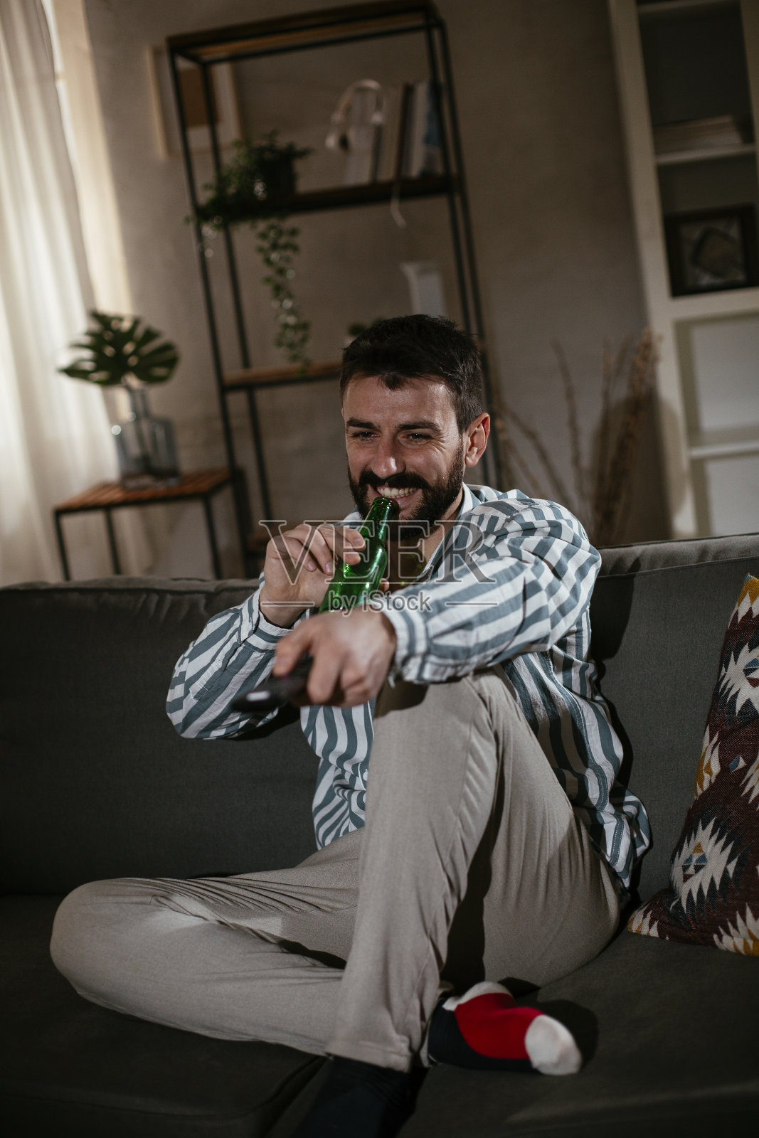 坐在客厅里看电影喝啤酒的男人。照片摄影图片