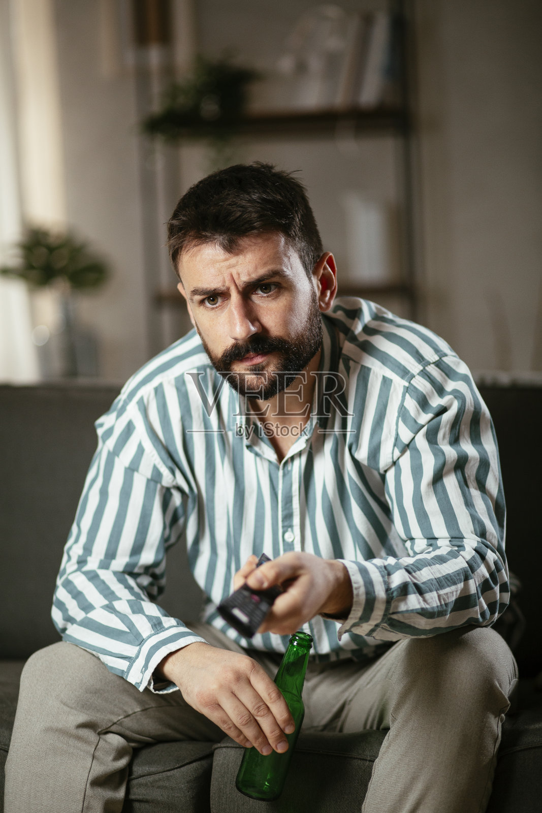 坐在客厅里看电影喝啤酒的男人。照片摄影图片