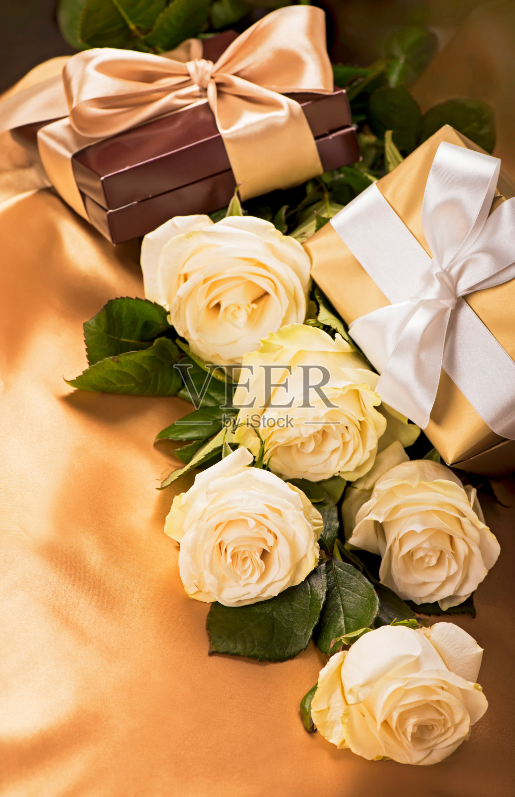 鲜花和礼物。金色丝绸背景上的白玫瑰照片摄影图片