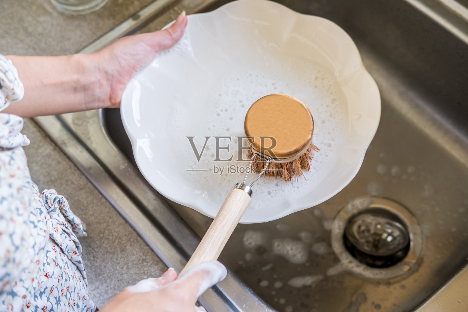 女人用手清洁白色的盘子和自然堆肥洗碗刷在水槽和流动的自来水。环保厨房和家居产品。零浪费、可持续、无塑料的生活方式照片摄影图片