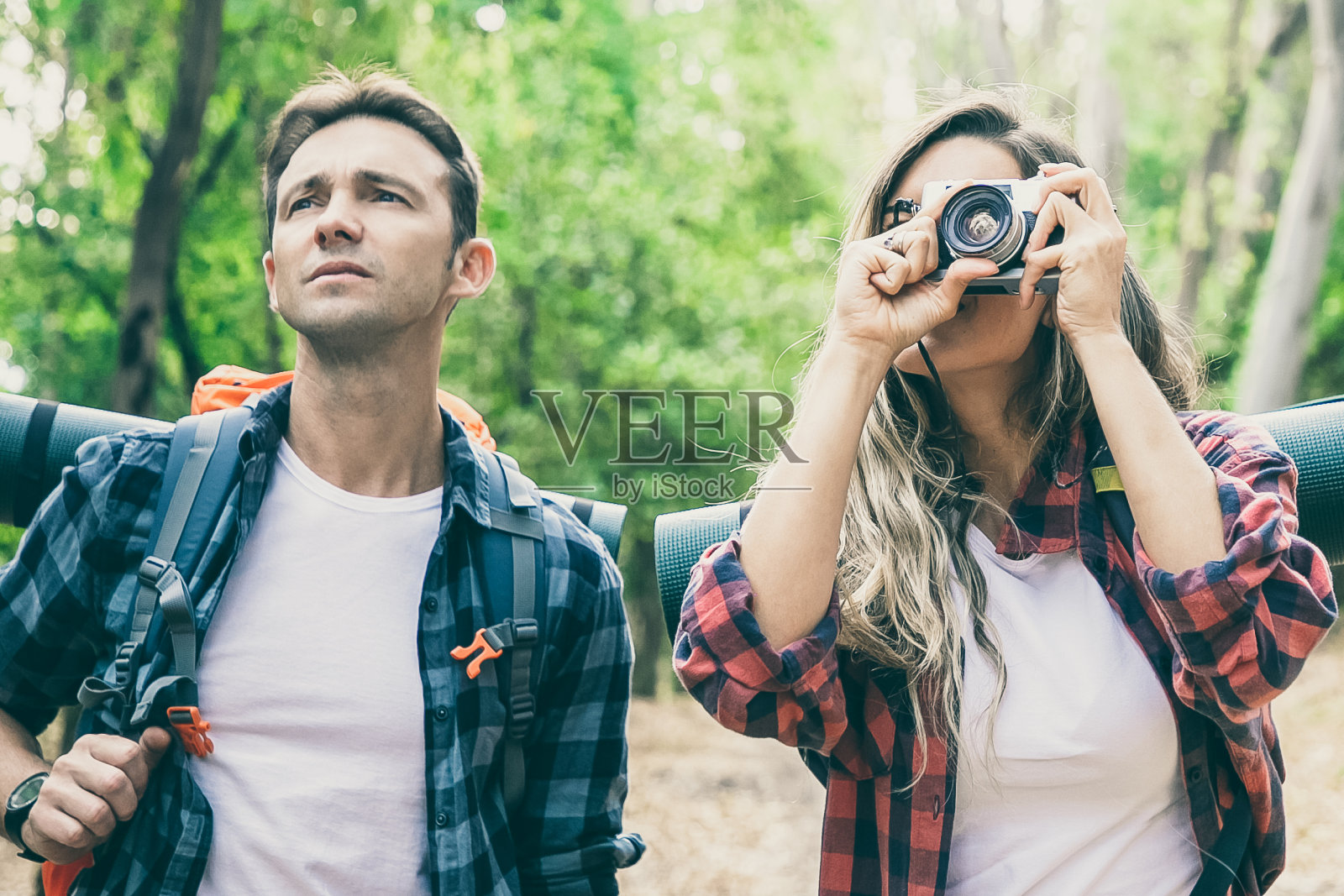 一对白种年轻夫妇在森林里徒步旅行，用相机拍照。体贴的男游客站在女人旁边看风景。背包旅游，冒险和暑期概念照片摄影图片