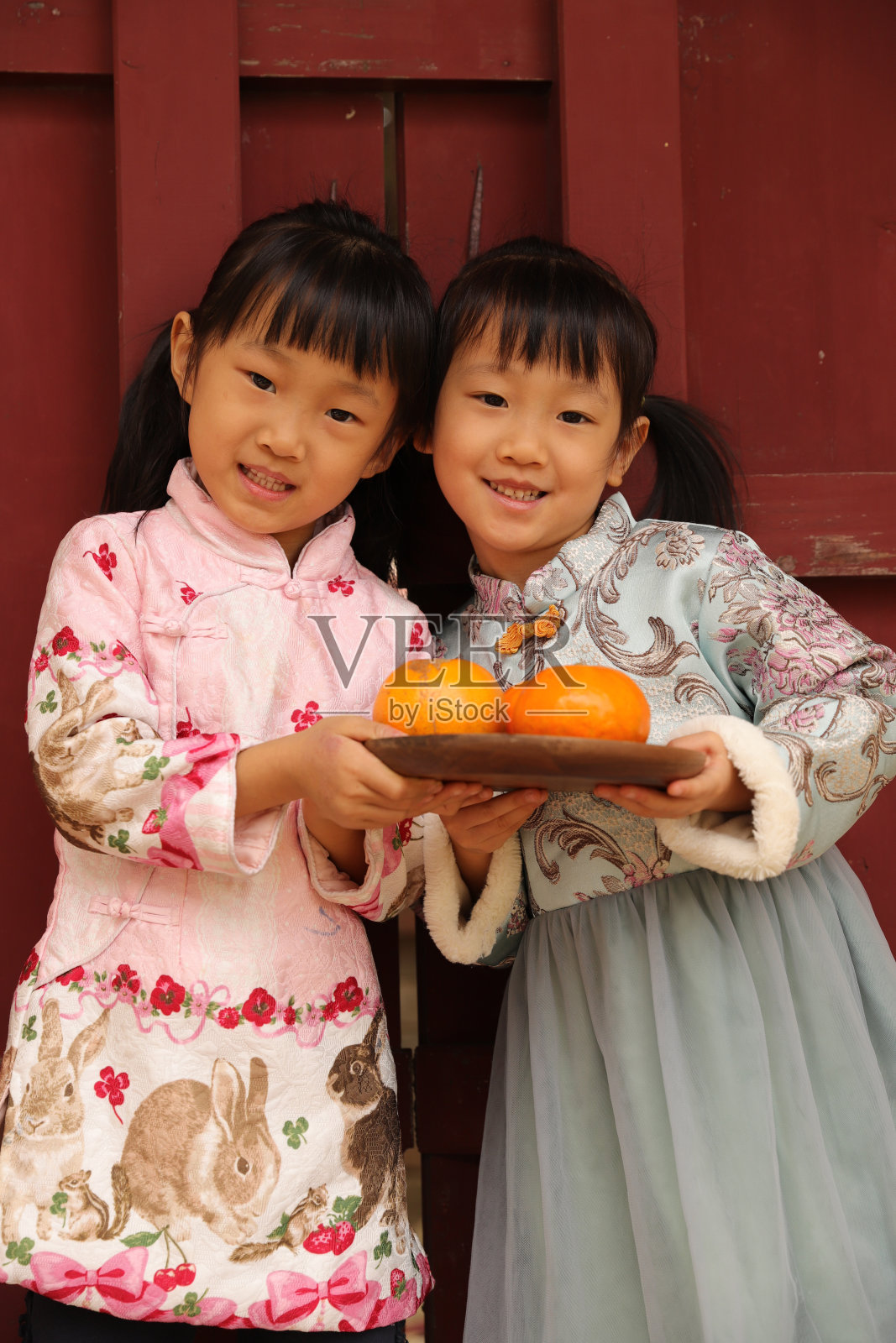 两个亚洲双胞胎女孩穿着旗袍在寺庙前进行新年访问。照片摄影图片
