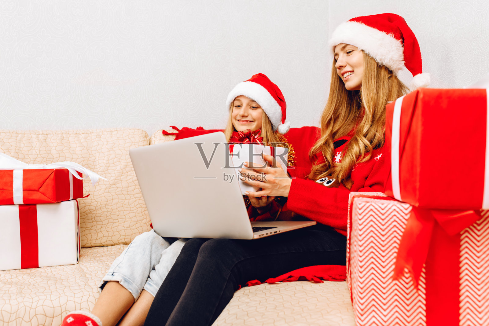 年轻的圣诞家庭，妈妈和小女儿，戴着圣诞老人的帽子，和朋友视频通话，在网上会议聊天庆祝新年，在家里的电脑上。照片摄影图片