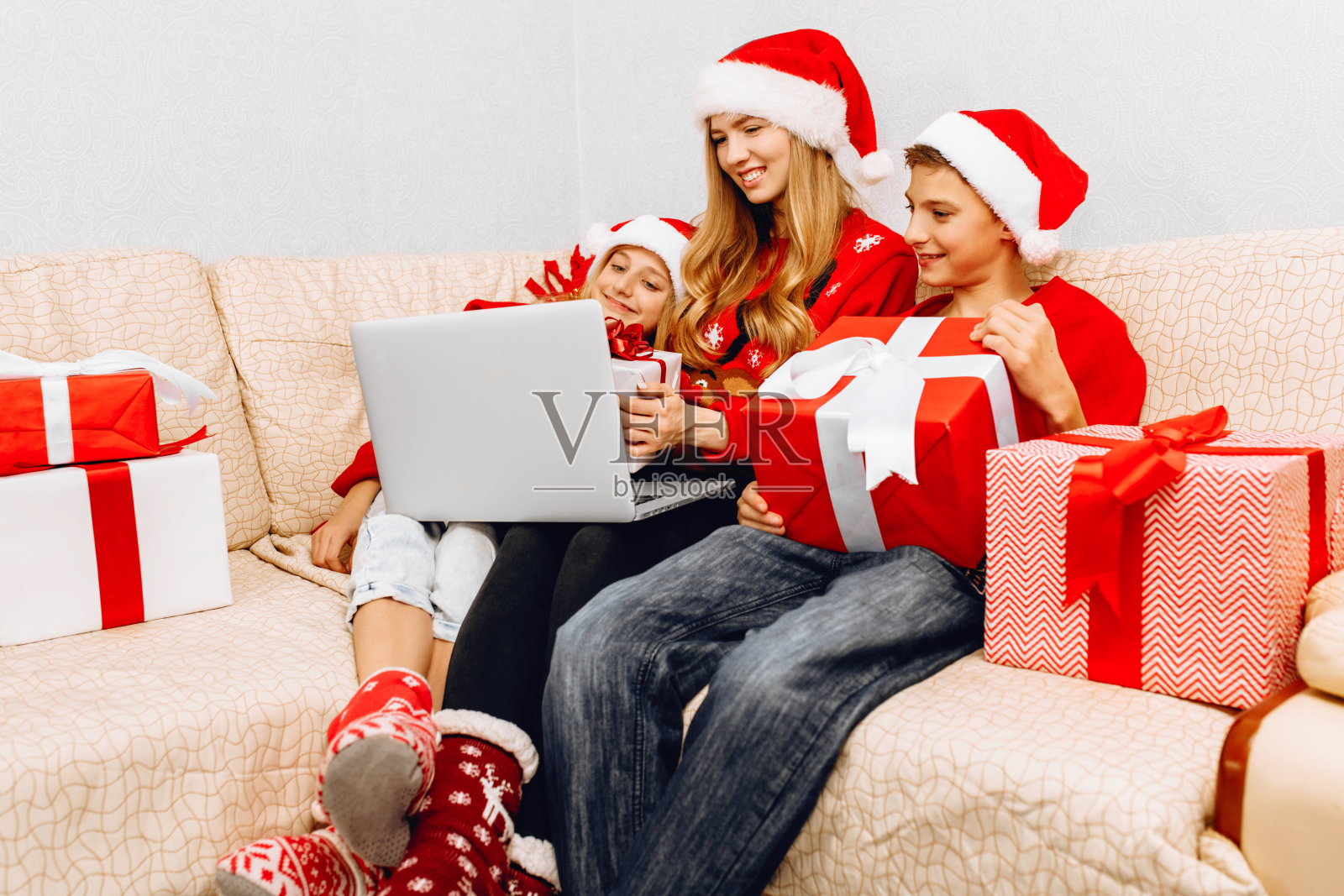幸福的一家人，年轻的妈妈和她的孩子们戴着圣诞老人的帽子，在家庆祝新年，坐在沙发上，打开圣诞礼物照片摄影图片