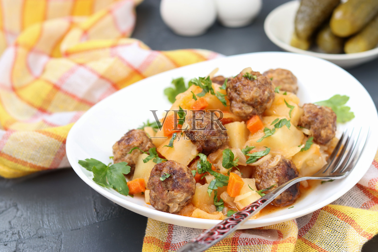 白盘子上炖土豆和肉丸，背景色为黑色照片摄影图片