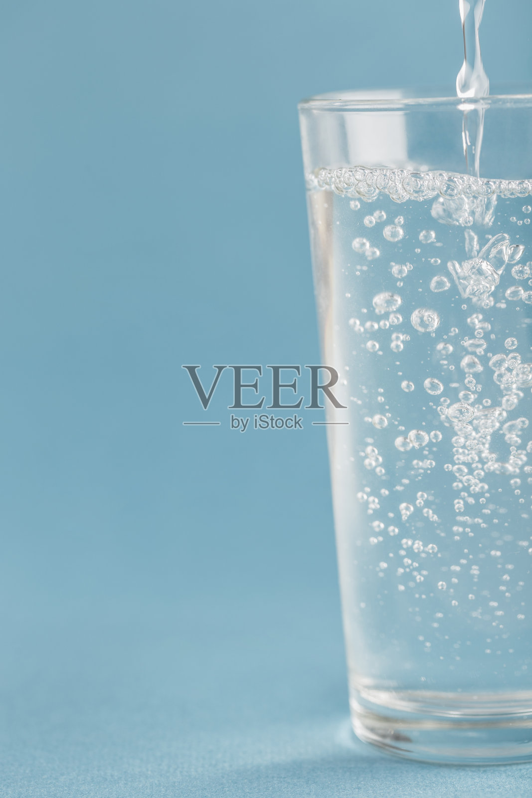 清水倒进一个蓝色背景的玻璃杯里。照片摄影图片