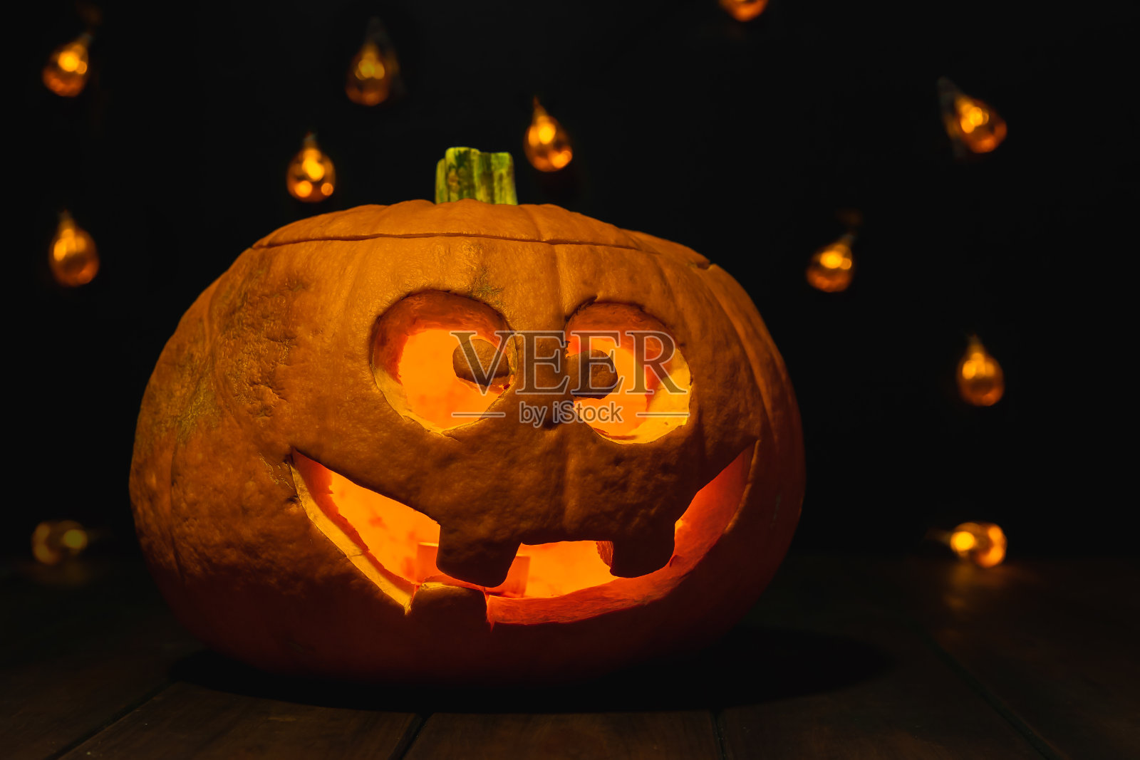 橙色南瓜和可怕的微笑。万圣节概念和恐怖场景的黑色背景与散景灯照片摄影图片