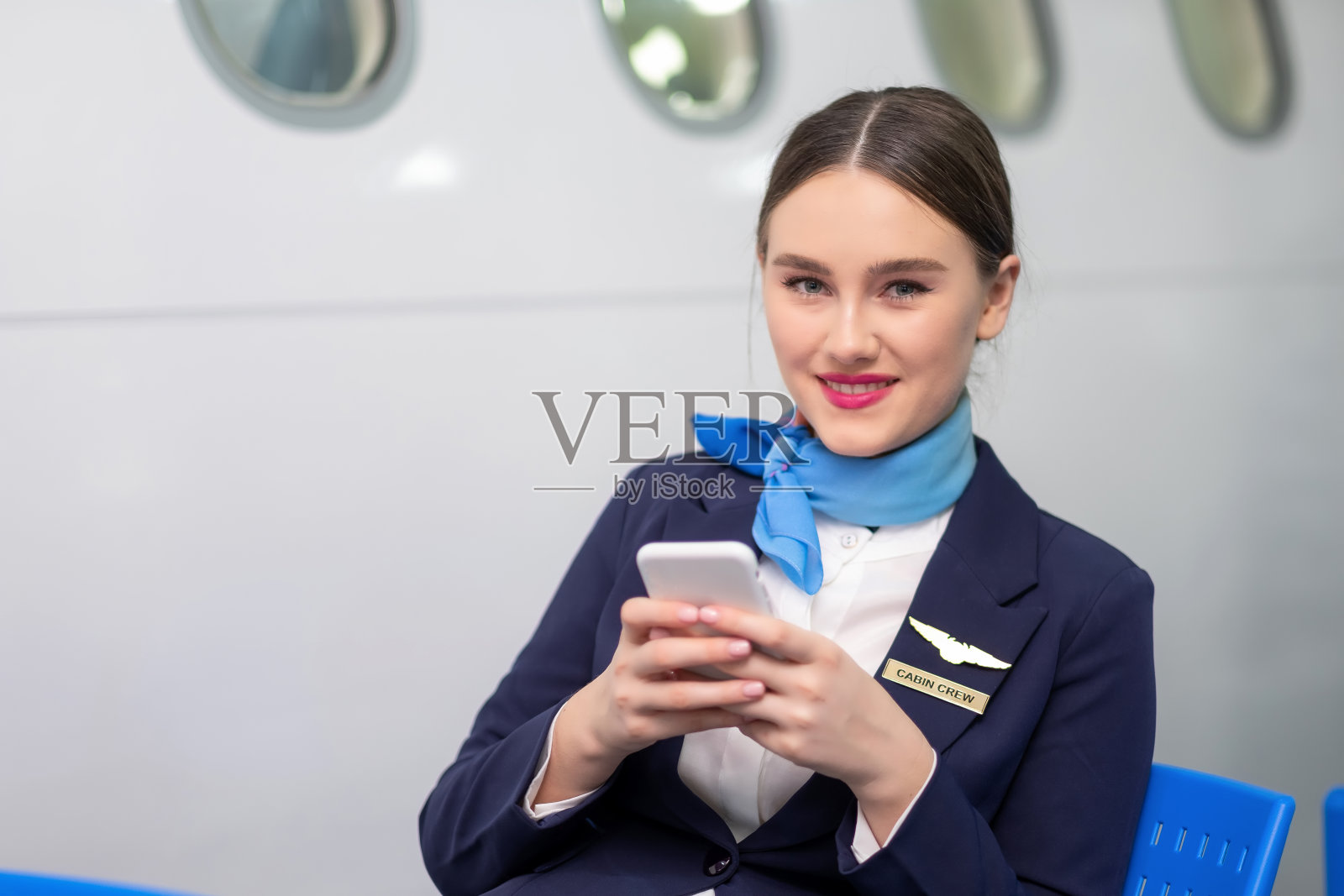 亚洲美女空姐在机场大厅玩智能手机。身穿蓝色制服，面带真诚微笑。社交网络、在线和商业概念。照片摄影图片