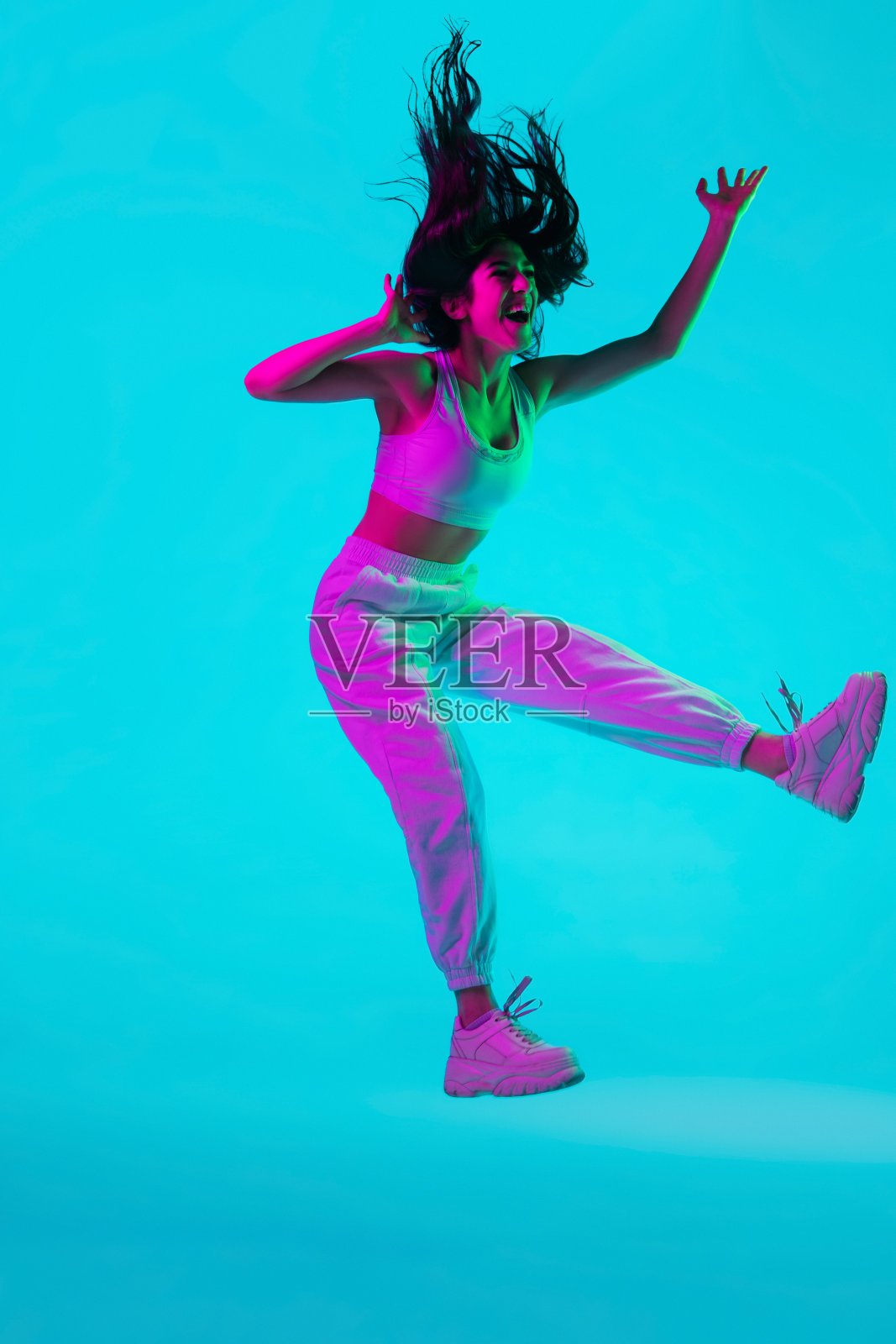 黑发美人的肖像孤立在彩色霓虹灯的蓝色工作室背景。跳很高。飞行照片摄影图片