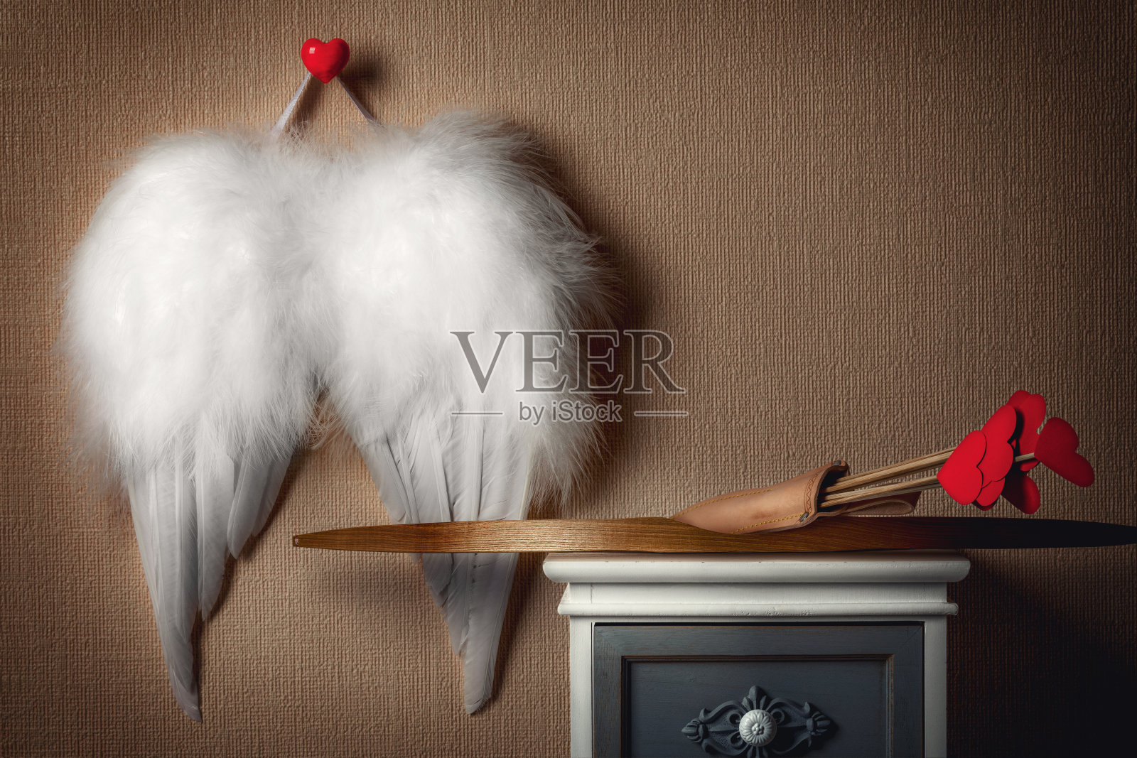 天使的翅膀挂在墙上。丘比特的武器把弓箭放在床头柜上。情人节的概念。照片摄影图片
