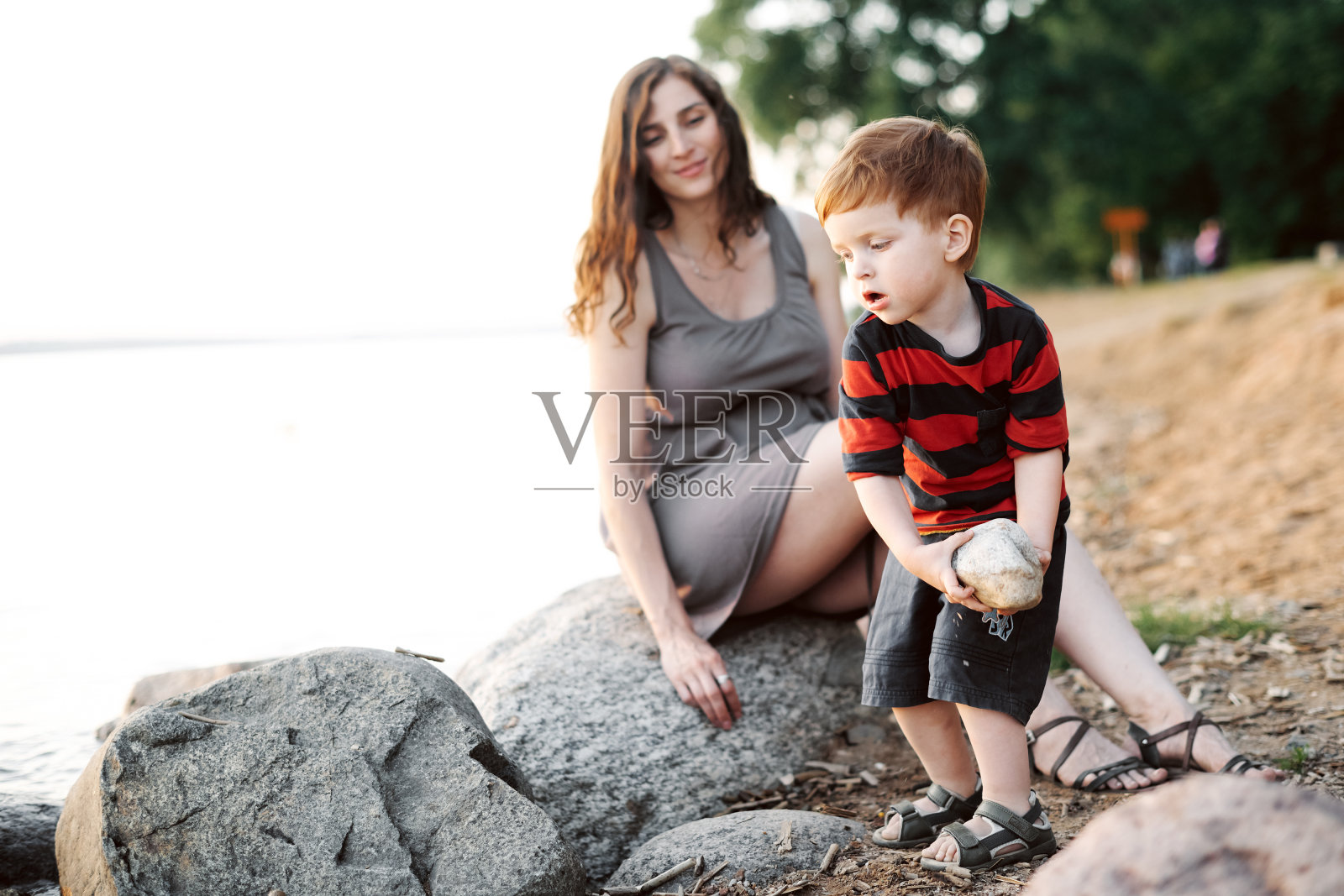 夏日日落时分，年轻的孕妇和她的小儿子在湖上玩耍照片摄影图片