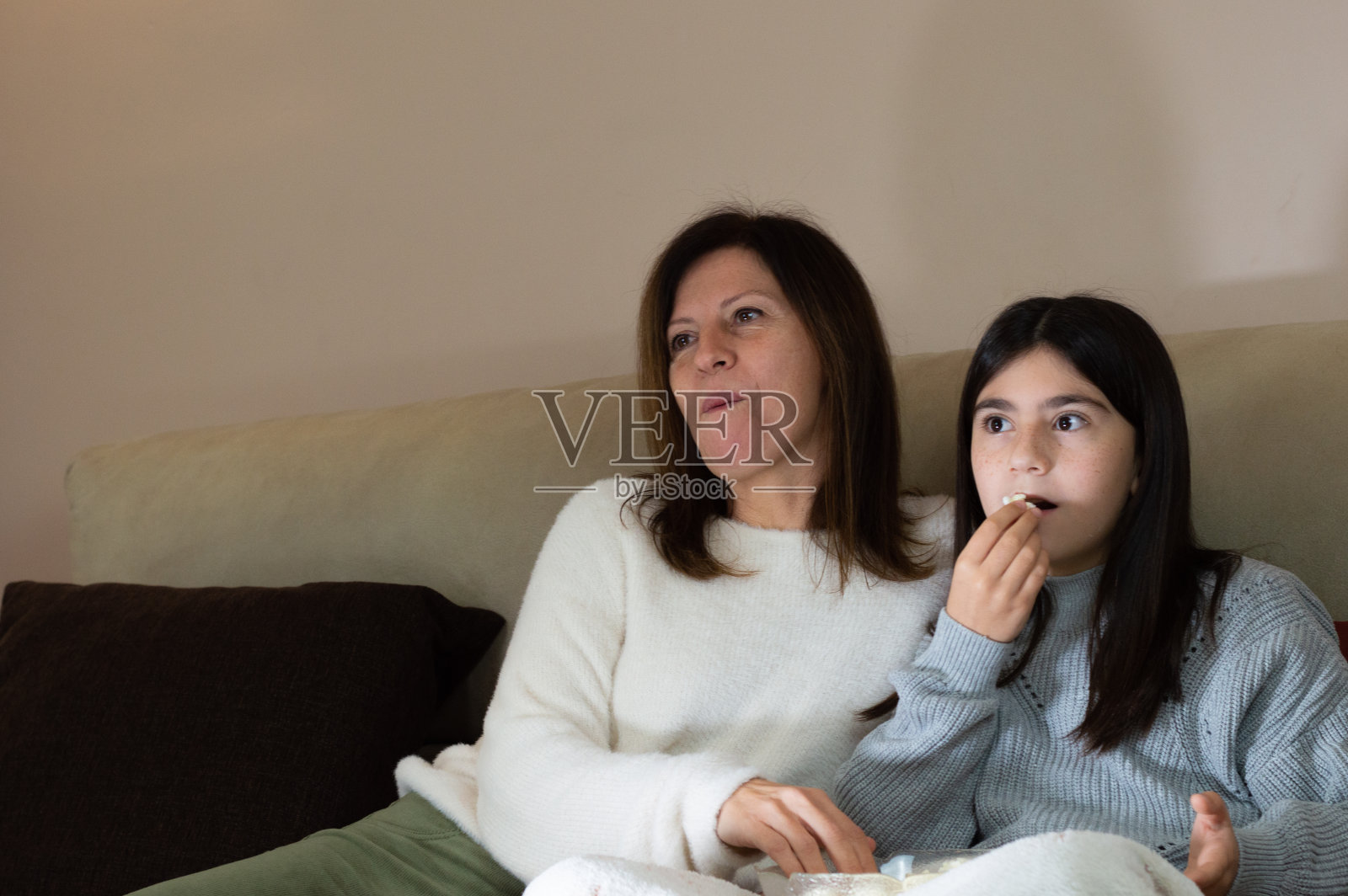 妈妈和小女儿在沙发上看电视，吃着爆米花照片摄影图片