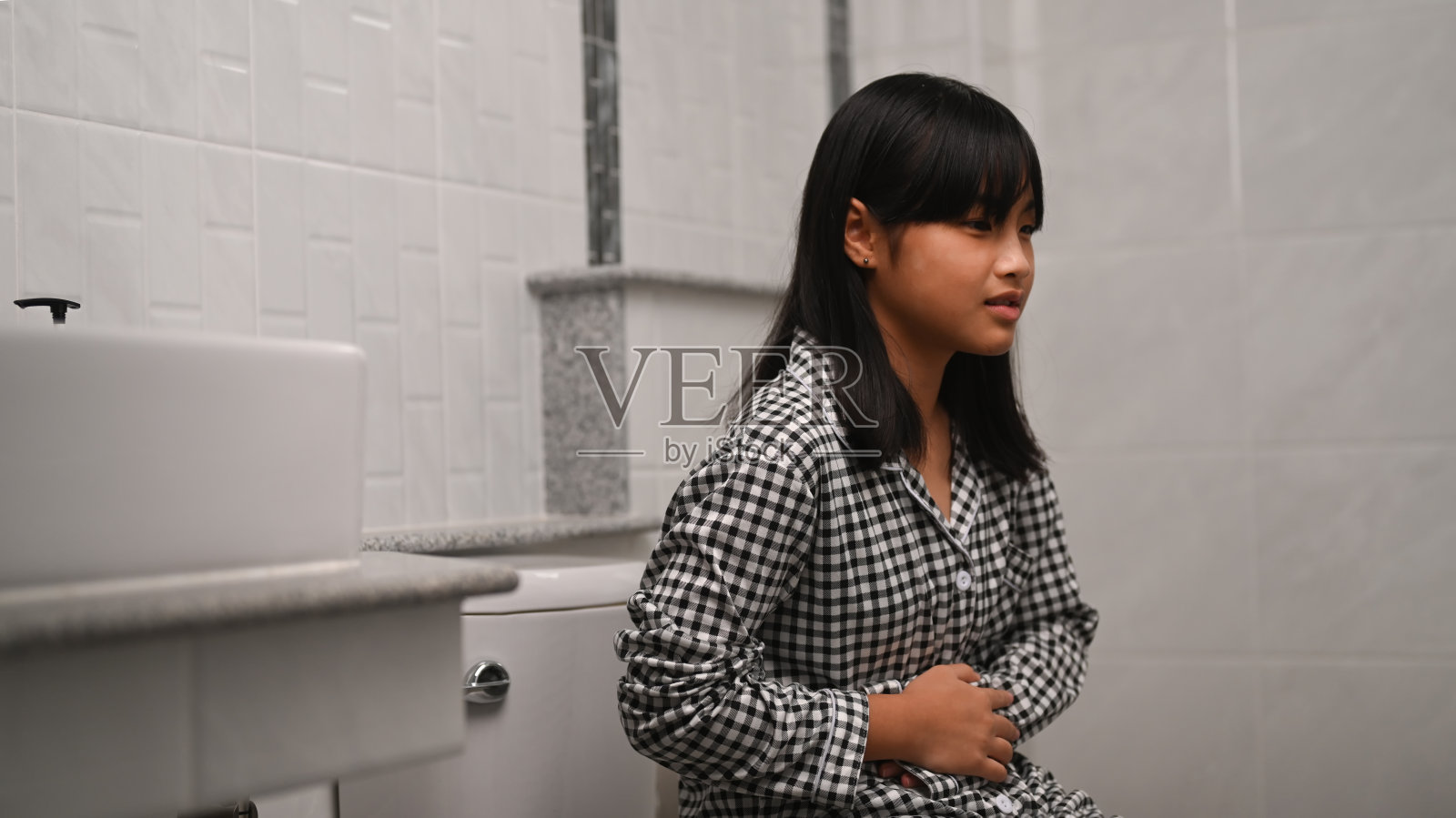 亚洲女孩抱着她的肚子，在家里坐厕所时肚子疼。照片摄影图片