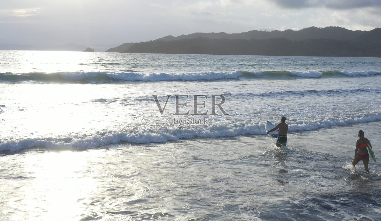 成熟的情侣走下海滩，带着冲浪板进入水中照片摄影图片