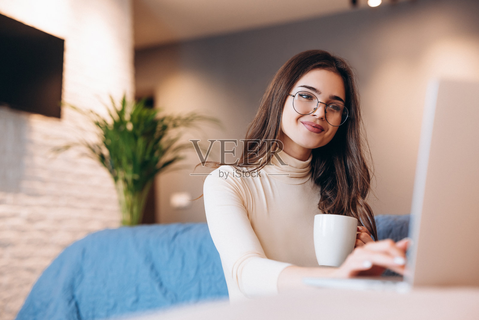 可爱的女孩戴着眼镜，喜欢在室内用笔记本电脑工作。女性自由职业者在家工作。学生室内照片摄影图片