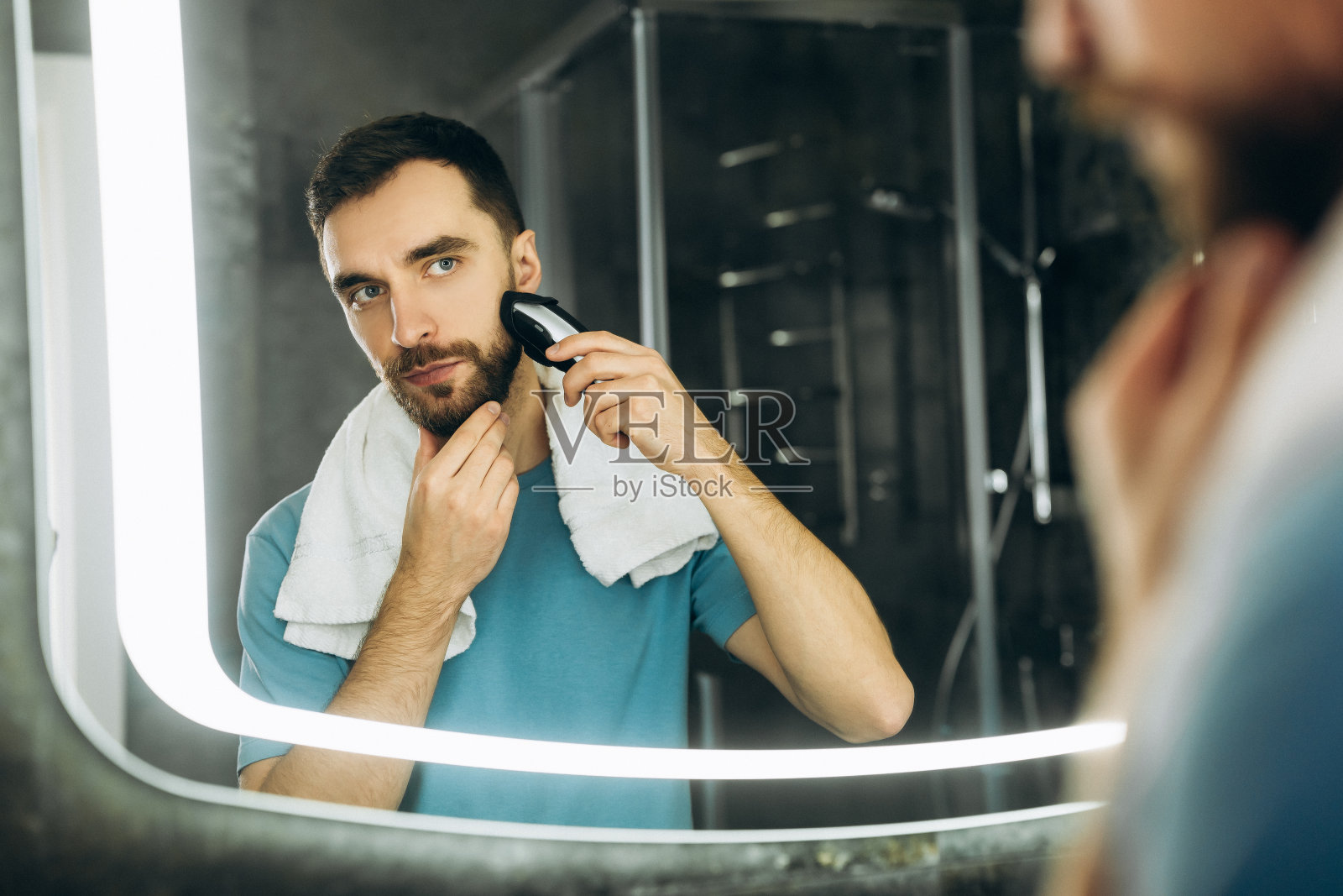 年轻有魅力的男人，用毛巾看着镜子和剃须清晨在家里。照片摄影图片