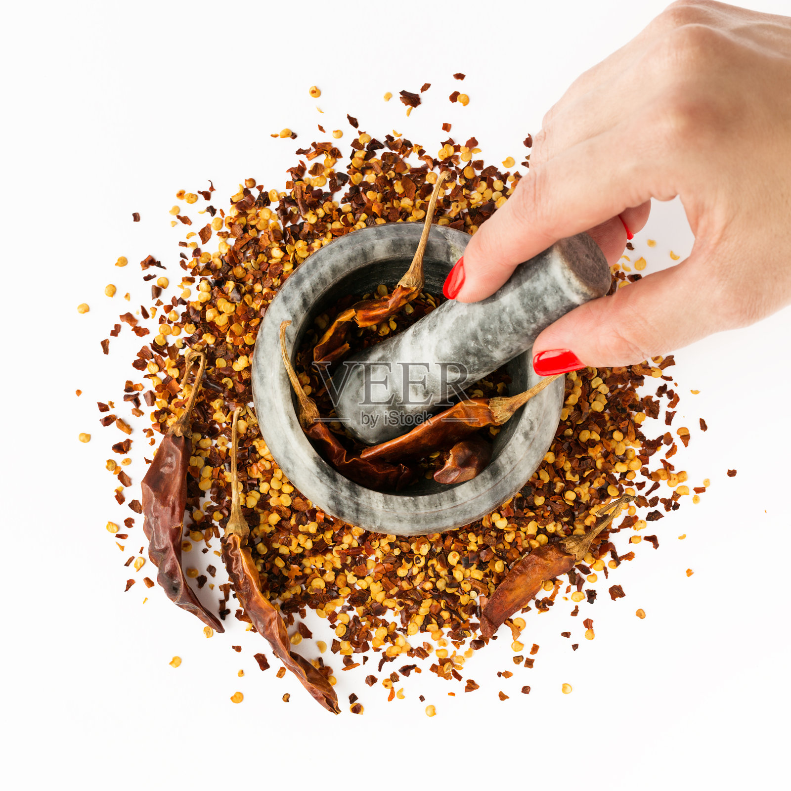石头臼碗里装满了碎红辣椒。女人手里拿着杵。干辣椒片和种子孤立在白色背景上。自制香料用于烹饪。照片摄影图片