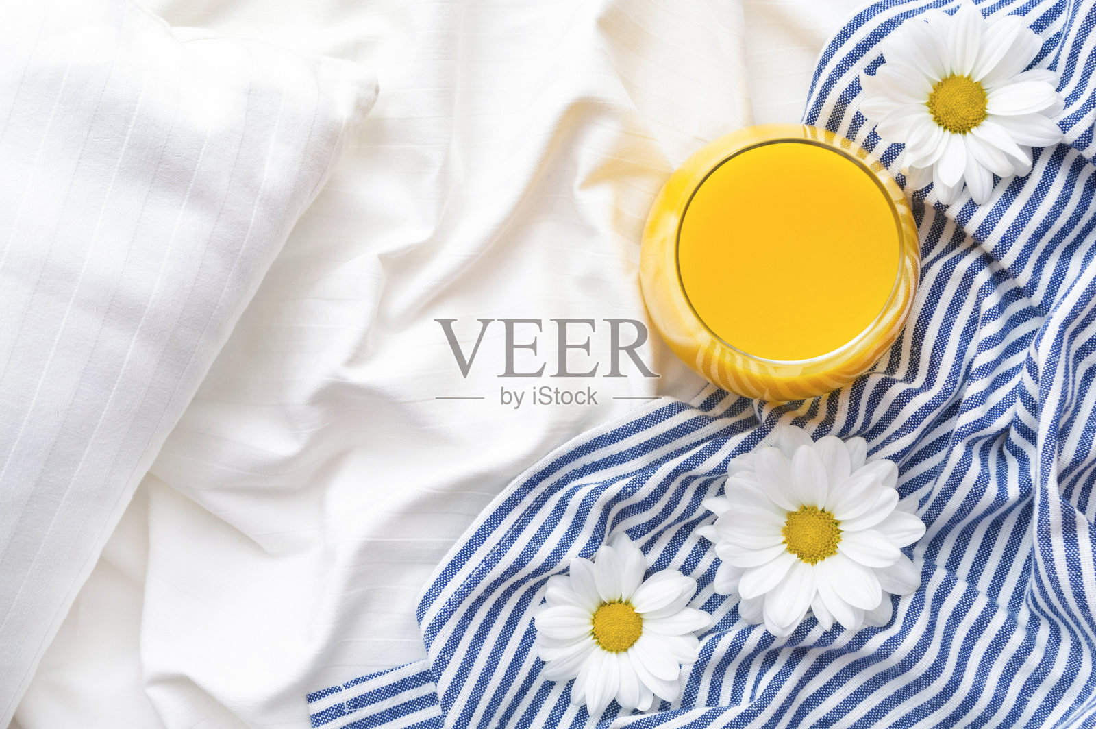 床上放着橙汁和洋甘菊花。照片摄影图片